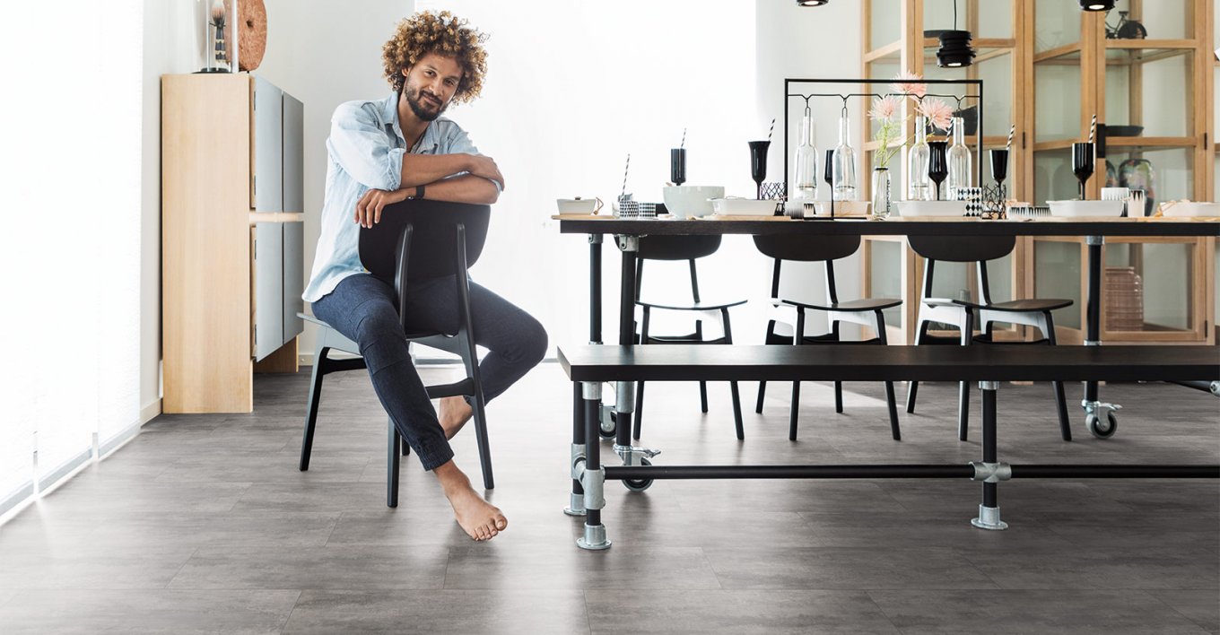 wineo Designboden mit Mann sitzend in der Küche mit Stuhl, Tisch und Schrank